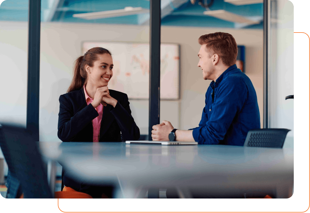 Two colleagues smiling and chatting across a table in a modern office.