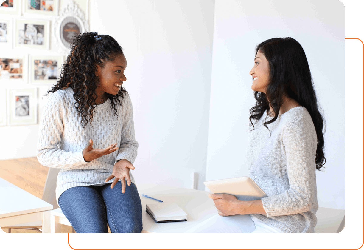 Two women engaged in a friendly conversation indoors.