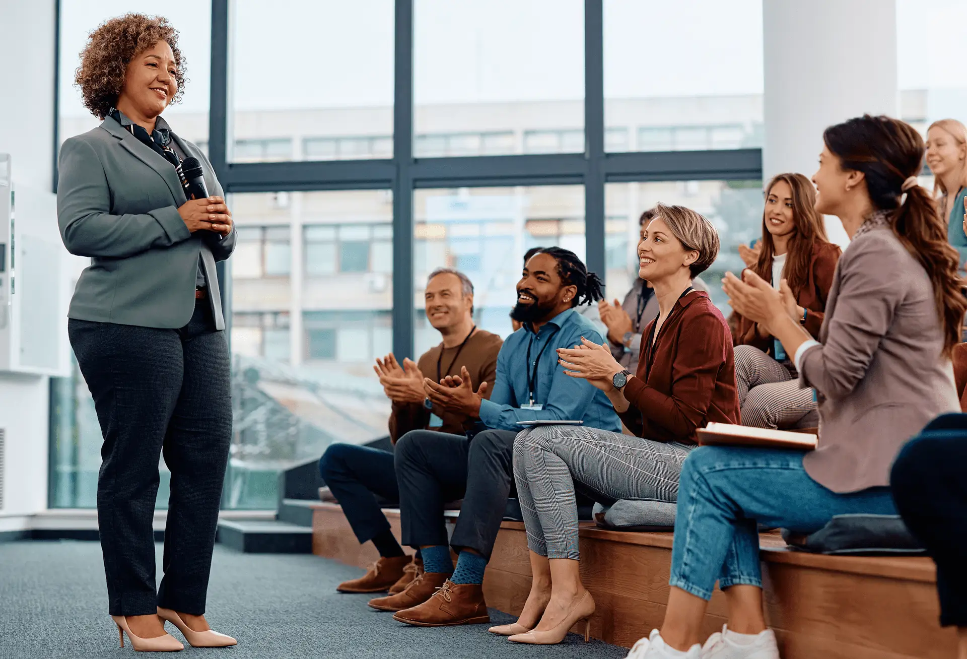 People attentively listening and applauding a speaker in a modern office setting.