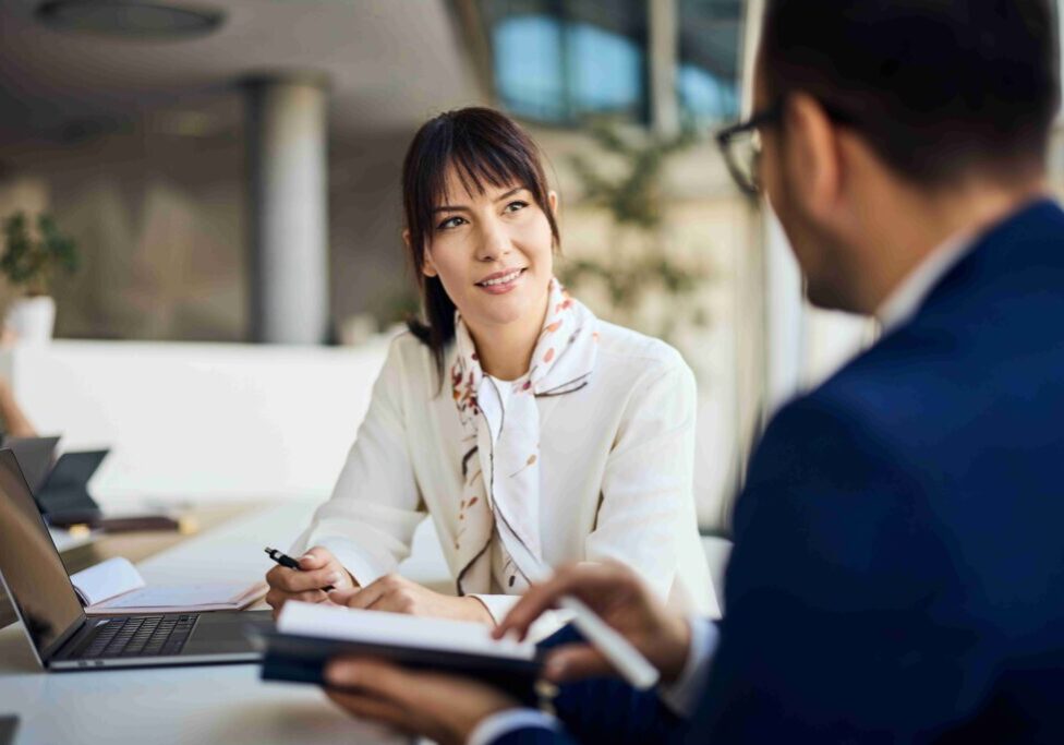 A woman in a white coat talking with a man during a consultation.