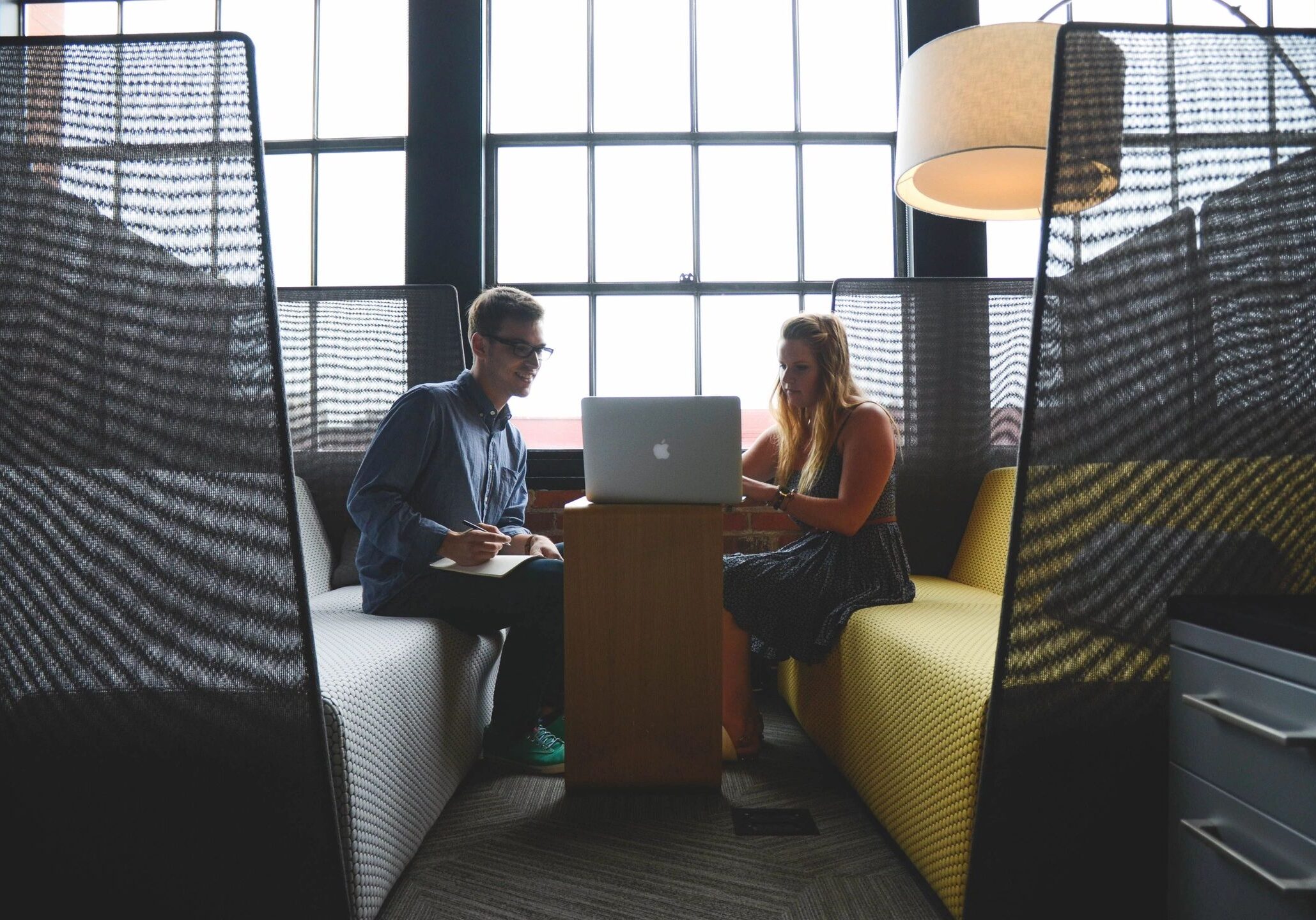 Two colleagues having a discussion in a modern office booth with a laptop.